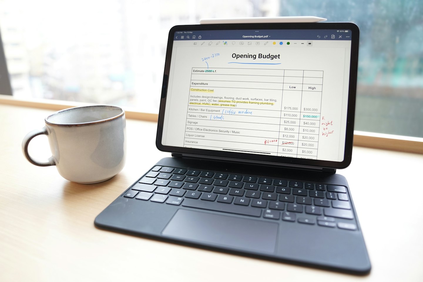 Tablet displays budget document with handwritten notes on desk.
